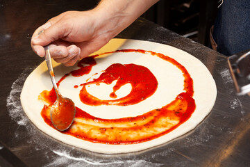 Cook making pizza or Focaccia, smears the tomato sauce over base