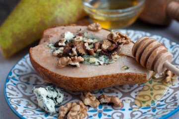 Pear baked with blue cheese, honey and walnuts on a plate on a gray background. Backed pear with  wooden honey stick. 