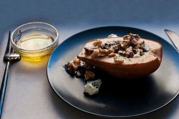 Pear baked with blue cheese, honey and walnuts on a black plate on a gray background. Backed pear with fork and knife
