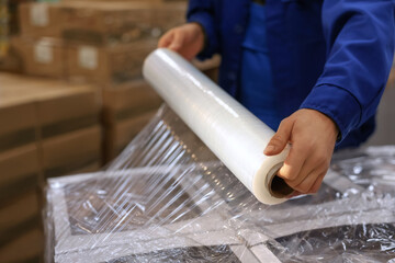 Worker wrapping boxes in stretch film at warehouse, closeup