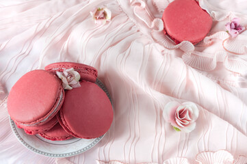 French macaroons on a plate on a pale pink tablecloth decorated with flowers. View from above