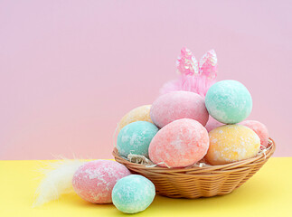 Multi-colored delicate painted Easter eggs with rabbit ears in a wicker basket on a pink-blue background. copy space.