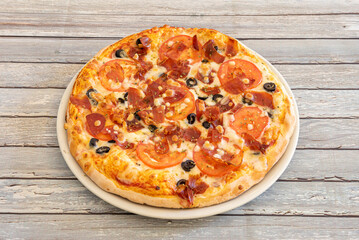 Pizza with melted cream cheese, pieces of serrano ham, black olives and fresh tomato slices