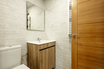Washroom with white exposed brick walls with wooden vanity unit and white porcelain sink