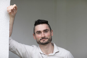 Young man with arm on a wall in a room looking pleased