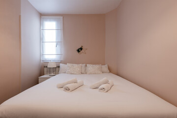 Fototapeta na wymiar Room painted in pale pink with a white bedspread bed and matching cushions with a small window on one side