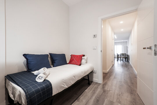 Small Pull Out Bed With Blue And Red Cushions And Blue Checkered Blanket Next To A Long Hallway