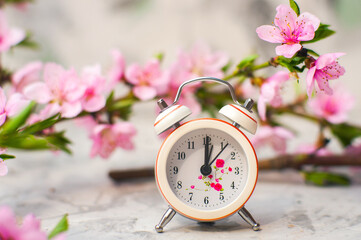 Miniature clock on background of flowering branch close-up and copy space. postcard for holiday. Beginning of spring..
