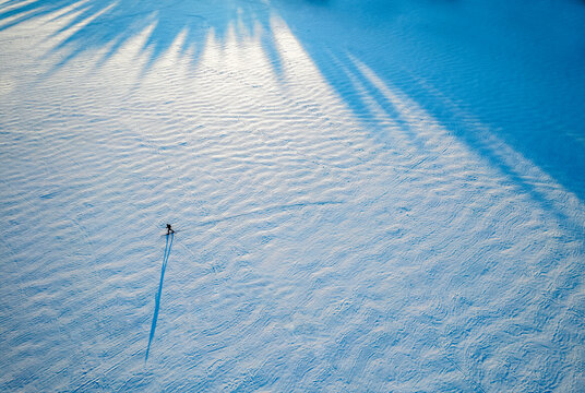 tiny figure and shadow of lone skier on frozen lake, Maine