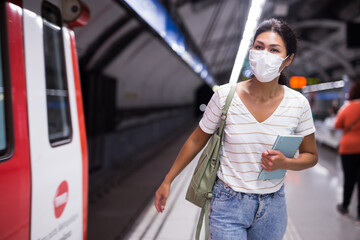 Oriental woman in face mask going along train in subway station.
