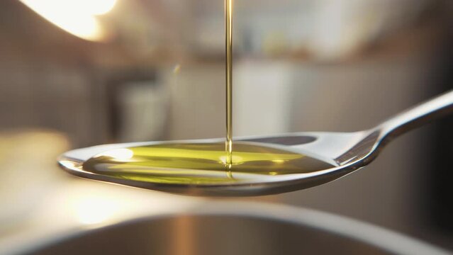 Macro shot of silver spoon filled with organic pure olive oil pouring over it.