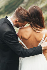 Close-up portrait of a groom kissing the shoulder of his bride standing with her back at camera wearing a dress with her back uncovered.