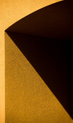 geometrical shapes angles from shadows cast on exterior orange cement concrete building or house wall in afternoon sun outdoors triangular pattern triangles and right angles vertical format backdrop
