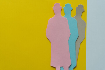 three paper dolls (one pink, one blue, one beige) on yellow paper with space