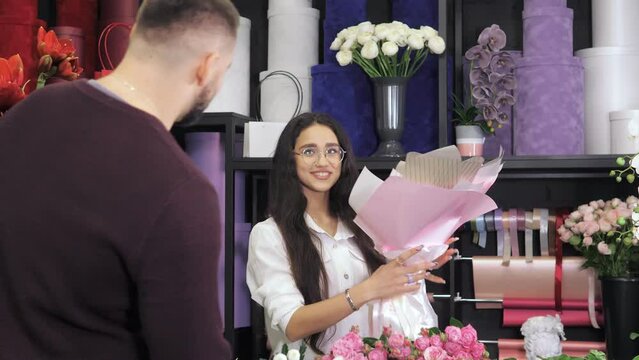 A young beautiful florist girl,the owner of a small business, sells a beautiful bouquet of flowers to a man.People,shopping,selling,floristry.Modern flower shop.Flower boutique.A hospitable saleswoman