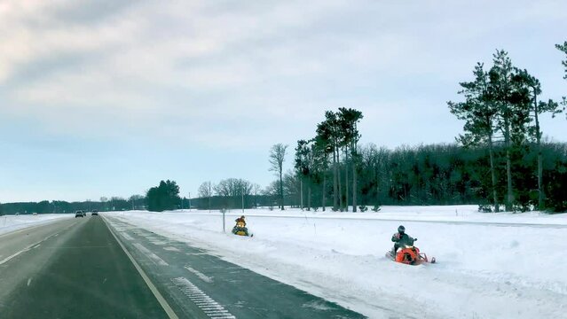 Snowmobiles approach in highway ditch as seen in POV clip through moving car windshield. Snowmobiling is a popular and fun winter activity in Minnesota.