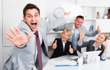 Fototapeta premium Excited businessman with happy team behind emotionally gesturing and celebrating victory at office