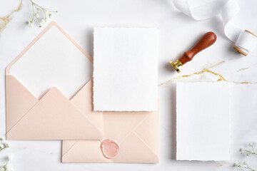 Elegant wedding stationery set. Flat lay pastel pink envelopes, blank wedding invitation cards mockups, silk ribbon, flowers on marble desk.