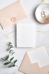 Wedding invitation mockup, pastel pink envelopes, golden rings, eucalyptus leaves on marble table. Elegant wedding stationery set. Flat lay, top view.