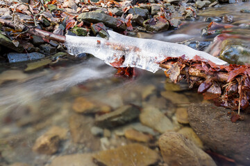 Ice on a branch above the surface of a flowing river.