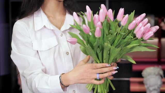 A young beautiful florist girl, the owner of a small business, collects tulips in a bouquet.The florist adds a new flower to the composition.People, buying, selling.Modern flower shop.Flower boutique.