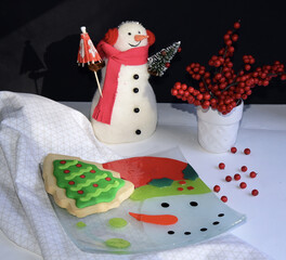A closeup shot of a snowman, Christmas cookie and holly berries