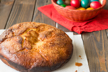 Kozunak (Traditional Easter homemade sweet bulgarian bread) and colored eggs in a red wicker basket on a table of wooden planks