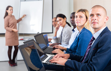 Obraz premium Side view portrait of multiethnic group of people sitting in row, working with laptops during business training. European man in focus of camera..