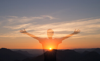 Man with arms raised with sunset in the mountains in the background. Person worshiping or thanking...