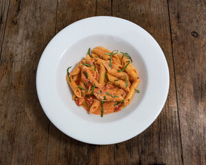 Pasta con salsa roja, tomate, albahaca y queso  mozzarella en un plato blanco sobre un fondo de madera