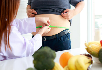 A female doctor or nutritionist checks the health of an obese person using a tape measure around the waist of an obese man. Weight loss concept. Medical services in hospitals.
