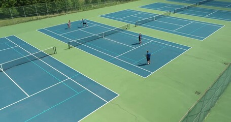 Four tennis players rally against each other on a park district tennis court in summer.
