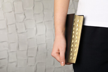 Woman holding Bible against white wall, closeup. Space for text
