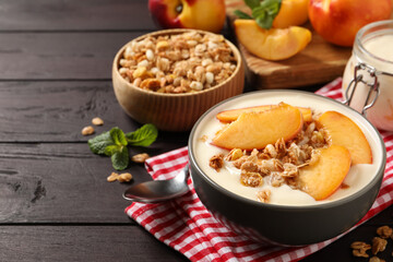 Tasty peach yogurt with granola and pieces of fruits in bowl on wooden table, space for text