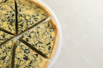 Plate of cut delicious spinach pie on light marble table, top view. Space for text