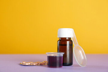 Bottle of cough syrup, measuring cup, dosing spoon and pills on color background. Space for text