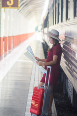 A woman stood beside the train holding a map with a red suitcase waiting for the train to leave the platform.