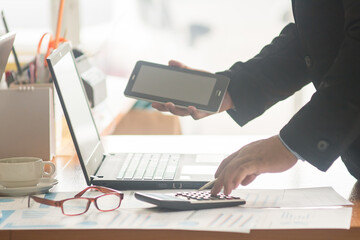 A businessman analyzing investment charts at workplace and using laptop and touch tablet.