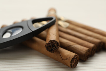 Cigars and guillotine cutter on white wooden table, closeup