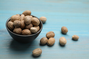 Bowl with nutmeg seeds on light blue wooden table. Space for text