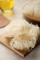 Board with uncooked rice noodles on wooden table, closeup