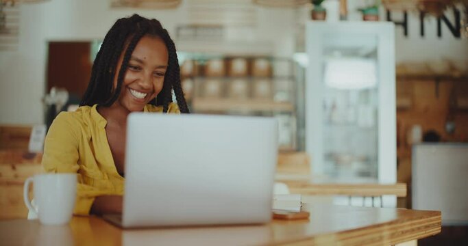 Successful young black woman working remotely in coffee shop on her laptop, success and diversity, future of remote work, young successful african american entrepreneur