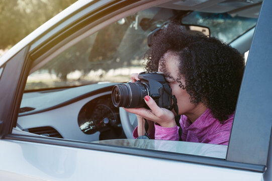 Close up image of female photographer with Afro hair style taking a picture by camera while sitting in the car.