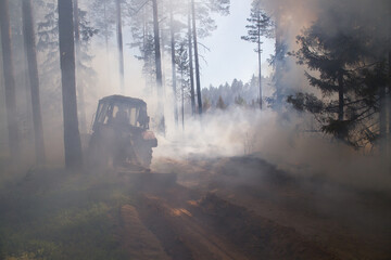Fototapeta premium A tractor makes a fire furrow during a forest fire. Strong smoke. Soft focus on the tractor.
