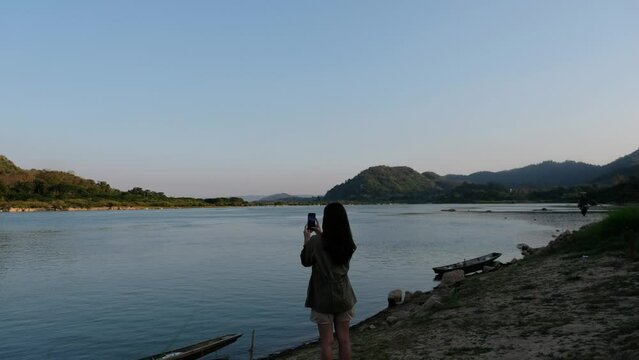 A young asian woman using mobile phone to take photo of he Mekong river