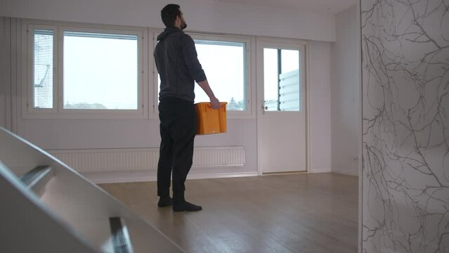 Man walks through empty new house and picks up a box to unpack. Moving house concept. Static shot.