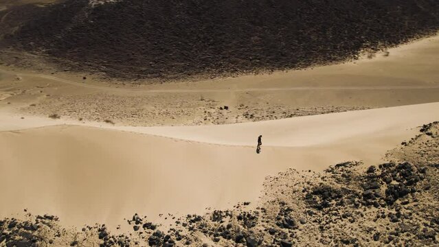 Man walks up ridge of a high sand dune in hot desert; aerial orbit