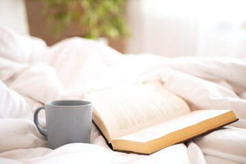 Fototapeta na wymiar Morning. A book and a mug of coffee and tea on the bed. Sunlight in the window. Comfort. Atmosphere. Lifestyle