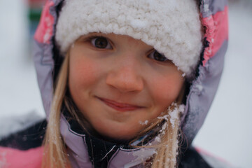 Close-up portrait of happy blond pretty preschool girl wearing bright colored snowsuit and white...