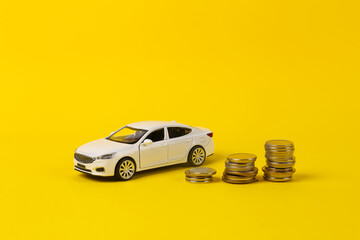 Toy car model with a stack of coins on a yellow background. Saving money, investing, buying car concept